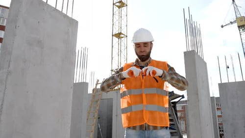 Foreman in protective helmet and vest stands at workplace in building and holds ruler