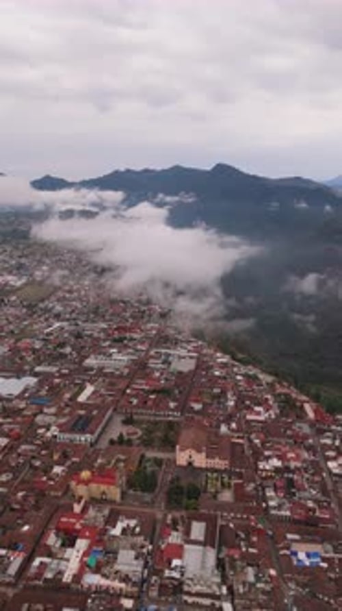 Vertical Bird's-Eye View Above a Village with Majestic Cloudy Mountains Nearby in the Distance
