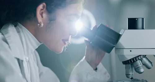 Female Scientist Looking Through Microscope in Bright Lab
