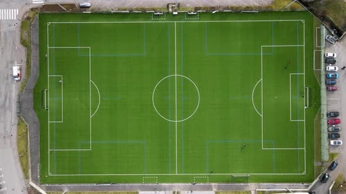 Top view of a green square football soccer field and some kids playing ball on it.