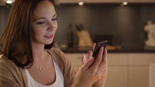Smiling Woman Using Smartphone in Home Kitchen