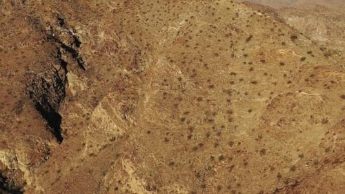 Drone shot rising slowly over barren desert mountain peaks.