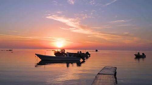 Beautiful colorful calm sea water at pier, and fisherman boats floating over twilight sunrise clouds