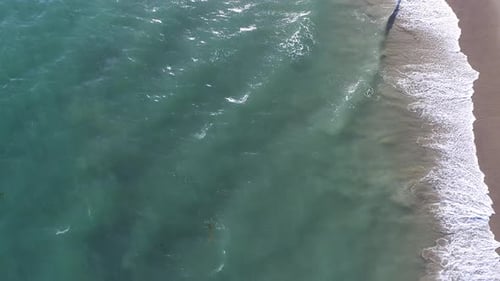 Aerial shot looking straight down at idyllic beach shoreline with waves rolling in on sandy beach