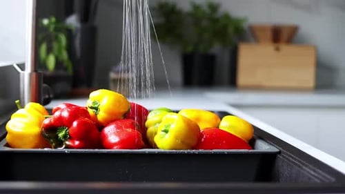 Yellow and red pepper are washed in a special tray for vegetables. The stream of water pours