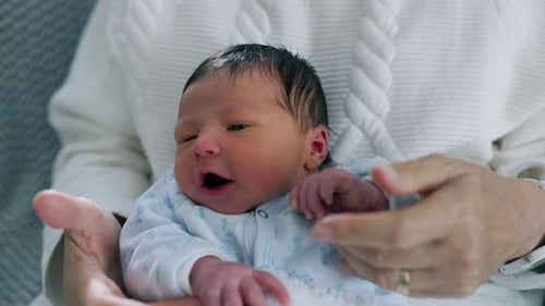 Senior Holding Newborn Baby in Arms Comfortably Indoors