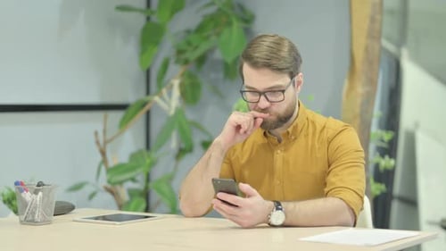 Man Uses Smartphone at Desk in Modern Office