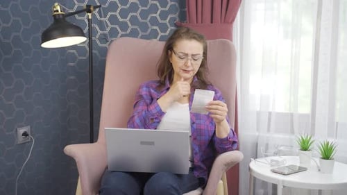 Woman Working on Laptop While Checking Finances at Home