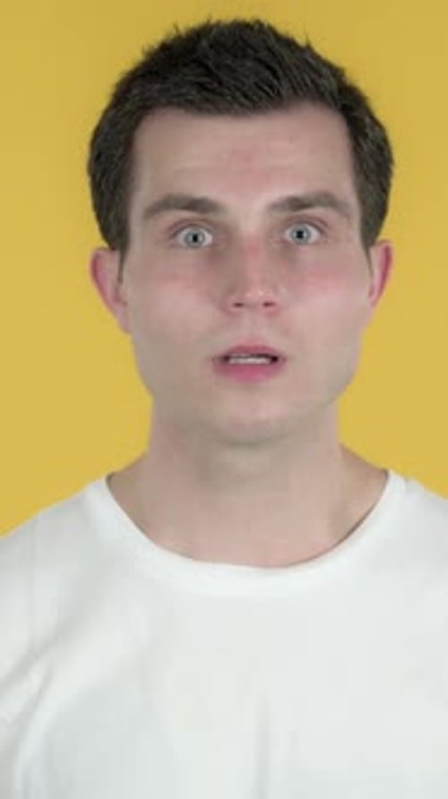 Shocked Young Man Covers Mouth on Yellow Background