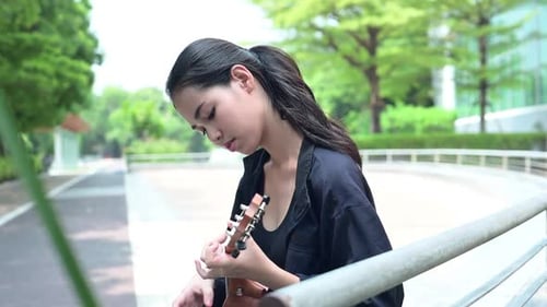 Teenage girl with holiday activities, Playing the ukulele in the park