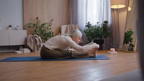 Senior Woman Stretching Legs on Yoga Mat Indoors