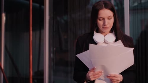 A businesswoman holds documents outdoors, portraying a freelancer, social media manager, or office