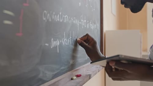 Person Writing on Chalkboard in Classroom Setting