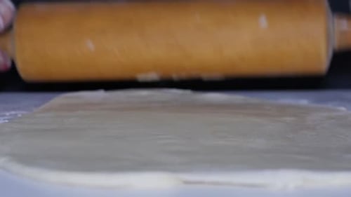 Extreme close-up of a woman rolling out pizza dough at home in the kitchen while making a homemade p