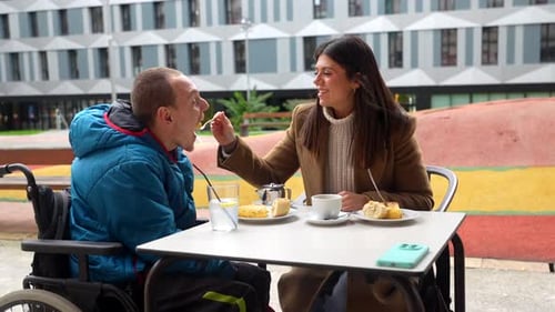 Woman feeding man in wheelchair dessert outside