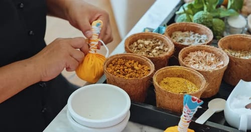 Hands tying yellow herbal compress ball in spa setting