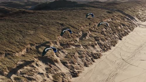Four paragliders soar along coastal dunes of Castricum beach, Netherlands. Drone