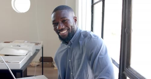 Smiling businessman sitting at desk, working on laptop in modern office