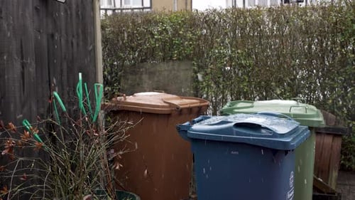 Light Snow Falling On Refuse and Recycling Bins In Front Garden Beside Hedge. Slow Motion