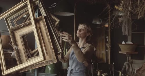 Mature female shop owner working in antique store arranging picture frames