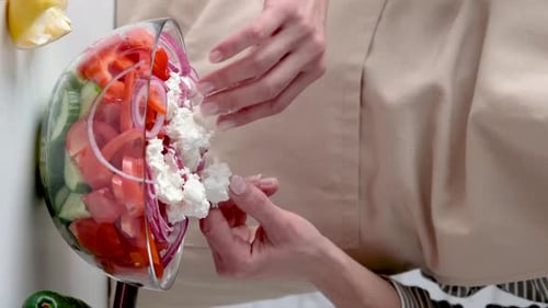 Femme ajoutant du fromage feta à un bol de salade grecque