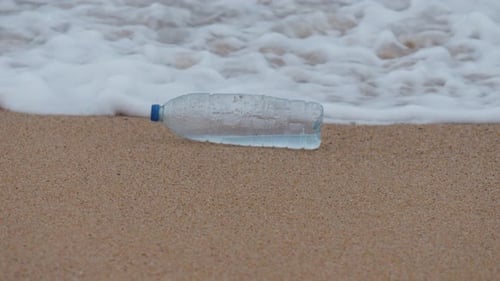 Plastic bottle on the beach, pollution, garbage, waves in slow motion, ecology, pollution