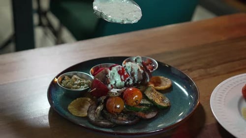 Chef pouring creamy white sauce with spoon on delicious meat plate with salad in restaurant