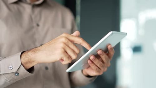 Close up of male hands holding digital tablet in business office. Businessman in a shirt is using