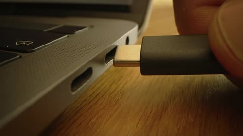 Close-up Macro Shot: Laptop on the Desk, Person Inserts USB-C Cable Adapter into Computer Port.