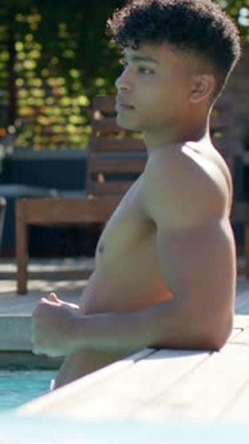 Vertical video: Opening eyes, shirtless man leaning on pool edge, turning head and scanning deck