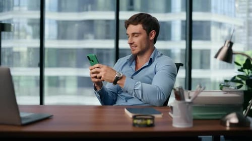Smiling Man Uses Phone at Desk in Office