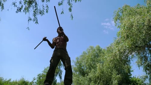 Muscular Man Practicing Martial Arts with Sticks Outdoors