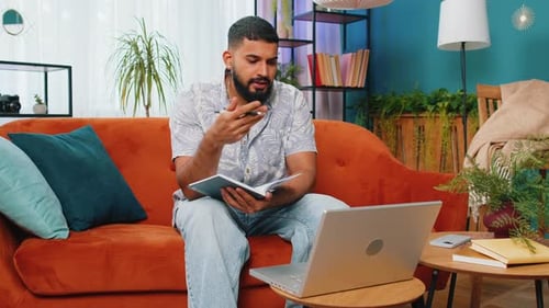 Man Writing in Notebook While Using Laptop at Home