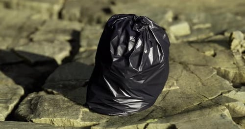 Using a Discarded Bag on Rocky Terrain By a Peaceful Waterbody at Dusk