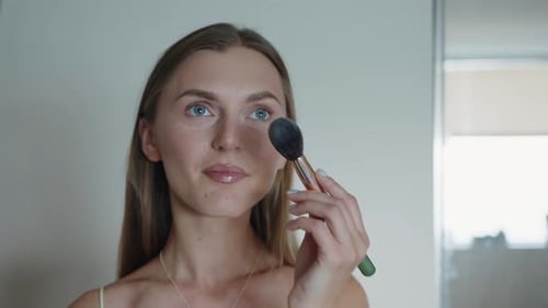 Woman Applies Makeup with Brush Indoors