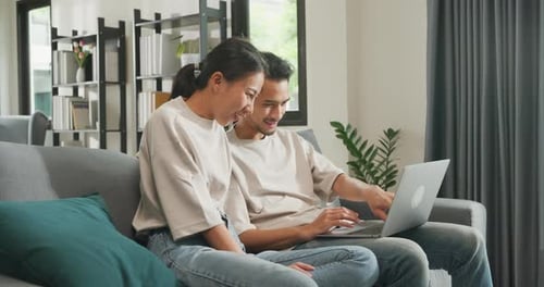 Smiling Couple Using Laptop on Living Room Sofa