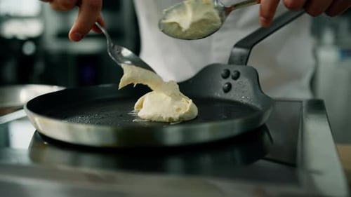 Der Vorgang des Einlegens des Teigs in die Pfanne - Der Koch brät Pfannkuchen in einer Pfanne.
