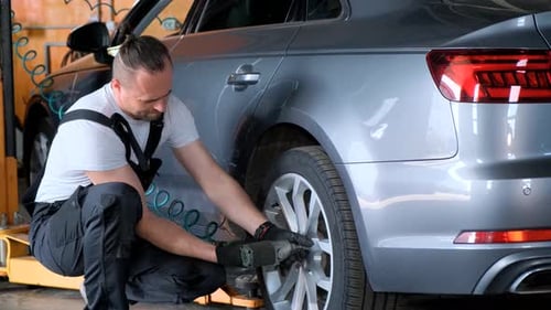 Man Changing Tire on Car in Garage Working on Wheel of a Motor Vehicle