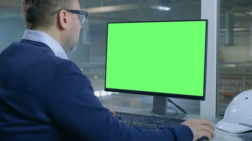 Der Chefingenieur arbeitet an seinem Computer mit Mock-up Green Screen. Das Innere der Fabrik ist von