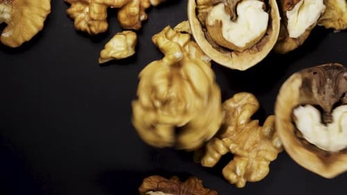 A peeled walnut rotates on a black background. The nuts are falling. Close-up. In move