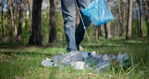 Un hombre con una bolsa de plástico recoge basura en el bosque calentándola con un palo