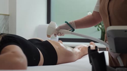 Cosmetologist Takes the Device and Starts Waxing the Woman's Legs in the Clinic
