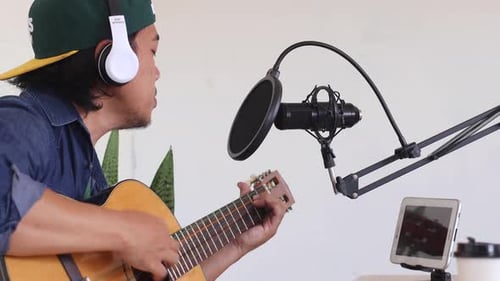 Asian influencer playing guitar during podcast or live video at home studio