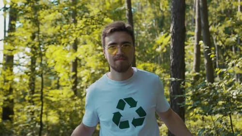 Un hombre con una camiseta blanca limpia un bosque recolectando bolsas de basura