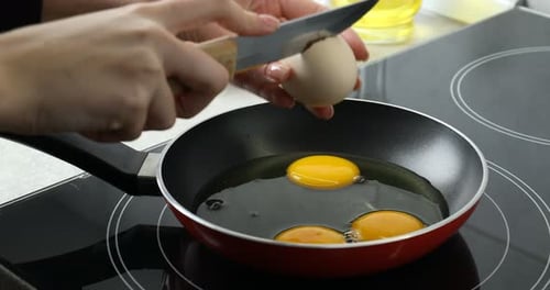 Femme cassant un œuf dans une poêle dans la cuisine, gros plan