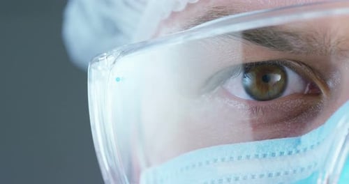 Un médecin ou un chirurgien portant un masque médical, un respirateur, des yeux bruns, des lunettes de protection, une casquette chirurgicale, un tuyau