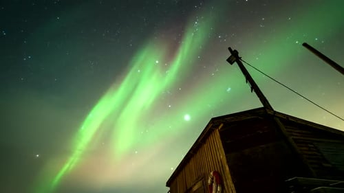 Mesmerizing northern lights flaring in sky over wooden boat house, time-lapse