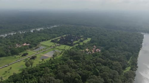 Iconic Angkor Wat temple stands amid sprawling jungle, encircled by water and greenery.