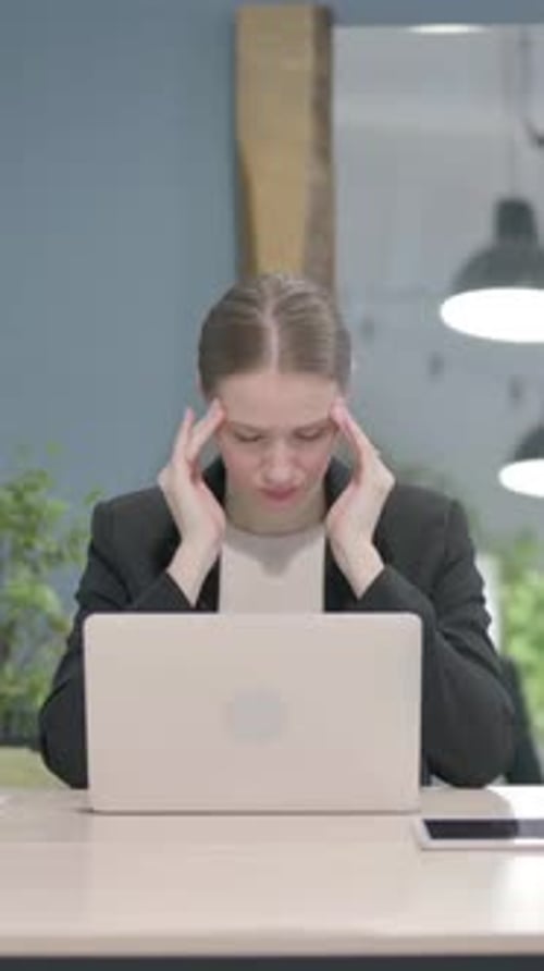 Businesswoman Massaging Temples at Desk in Modern Office