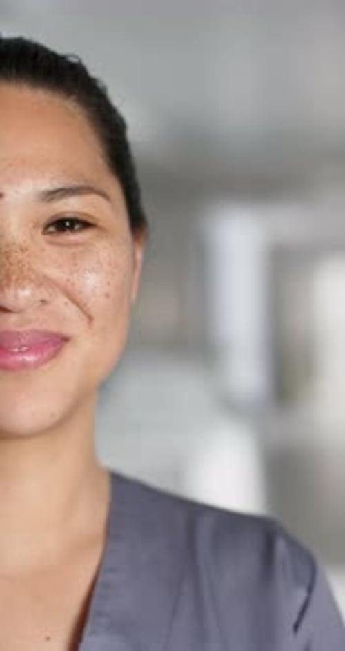 Vertical video of portrait of happy asian female doctor wearing scrubs in hospital, slow motion